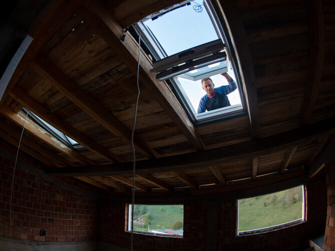 construction worker installing environmentally friendly and energy efficient roof window. Room under construction with wooden beams, boards and windows view from inside