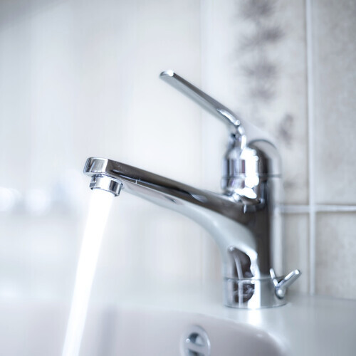 Shiny, chrome tap with running water stream inside apartment bathroom. Close up shot, shallow depth of field, no people
