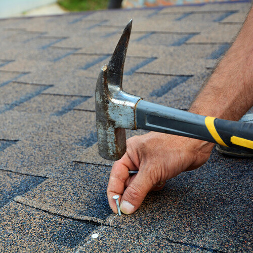 roofer nailing down asphalt shingle roofing