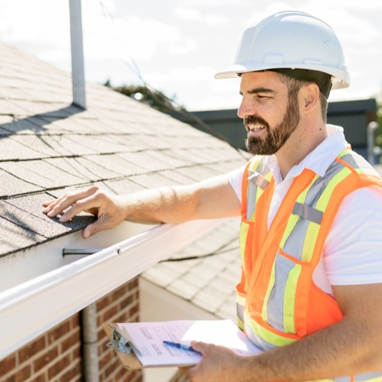 professional roofer inspecting a roof on a ladder with a clipboard smiling