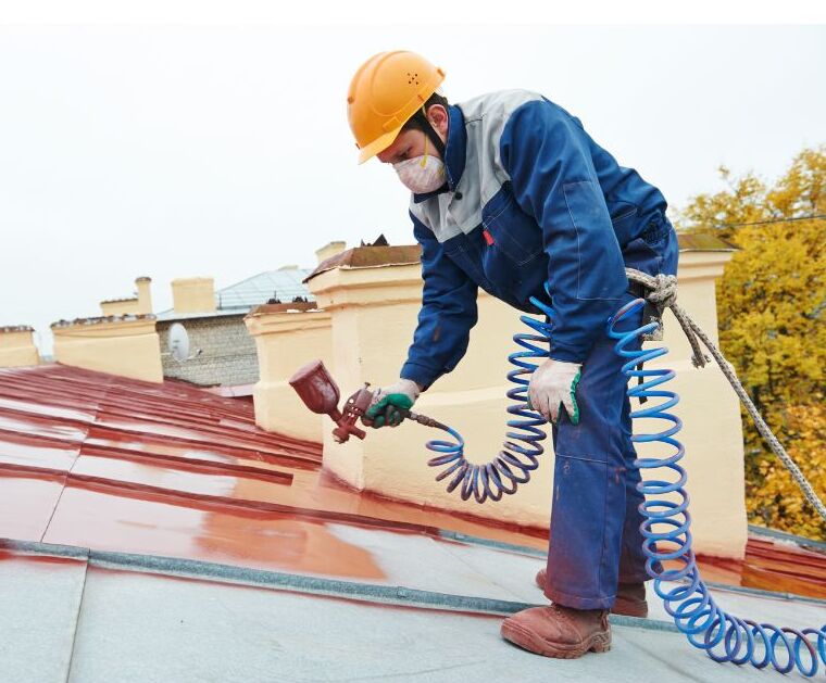 Worker sprays elastomeric coating onto a roof.