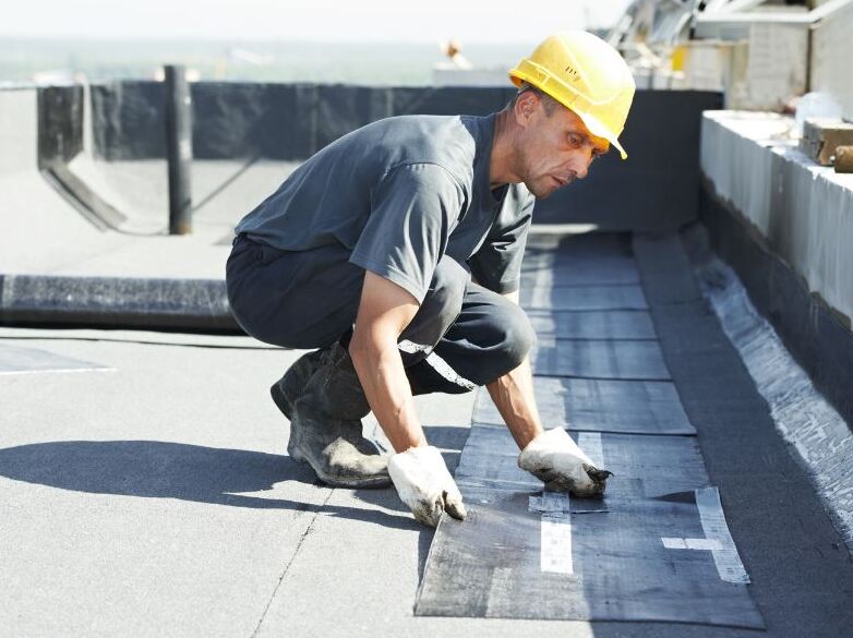 A worker is laying down silicone pieces on the roof.