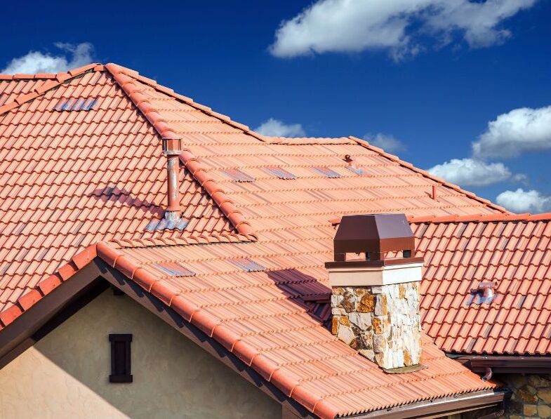 Red tile roof on a house with a blue sky in the background.